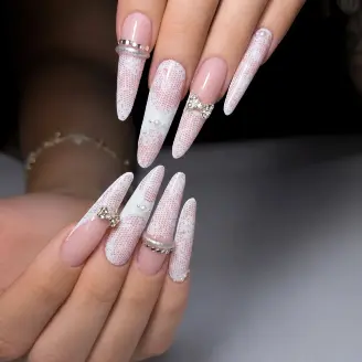 Dlouhé stiletto nehty s třpytivým bílo-růžovým ombré efektem, stříbrnými kamínkovými pásky a mašličkou.